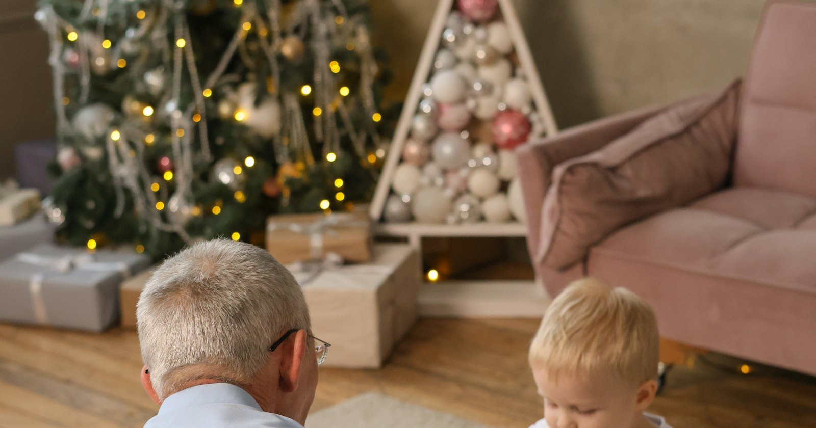 Abuelo y nieta abriendo juntos un regalo de Navidad junto al árbol